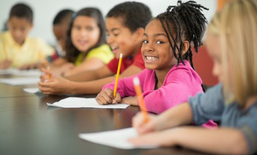 crianças sorrindo enquanto escrevem em sala de aula.
