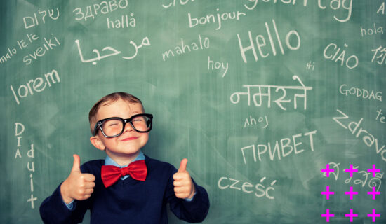 Menino sorri na frente de uma lousa com palavras em diversos idiomas.