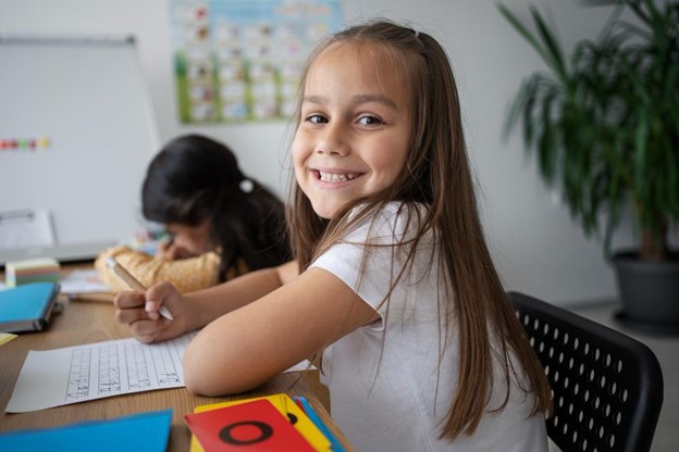 criança sorridente sentada à mesa fazendo atividades de alfabetização