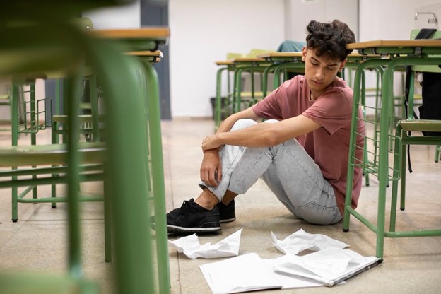 menino em escola com olhar triste para folhas caídas no chão pensando em evadir