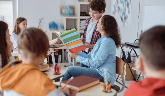 Professora no centro de uma roda de alunos aplicando a metodologia de sala de aula invertida.