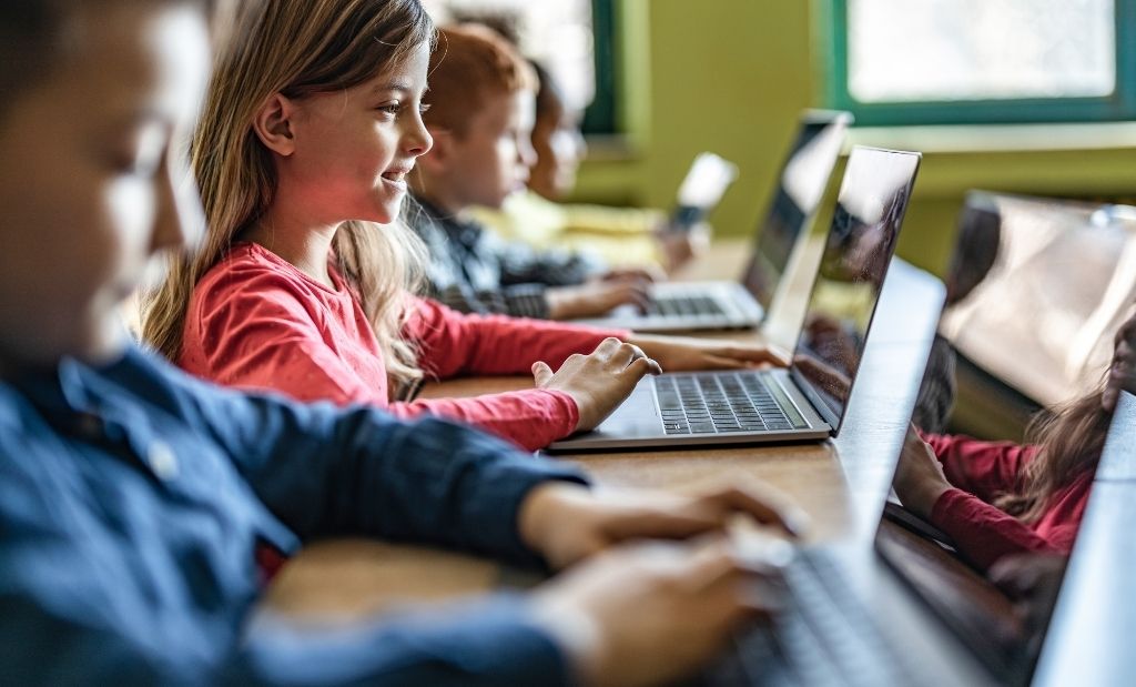 crianças usando laptops em uma sala de aula, aprendendo com tecnologia.