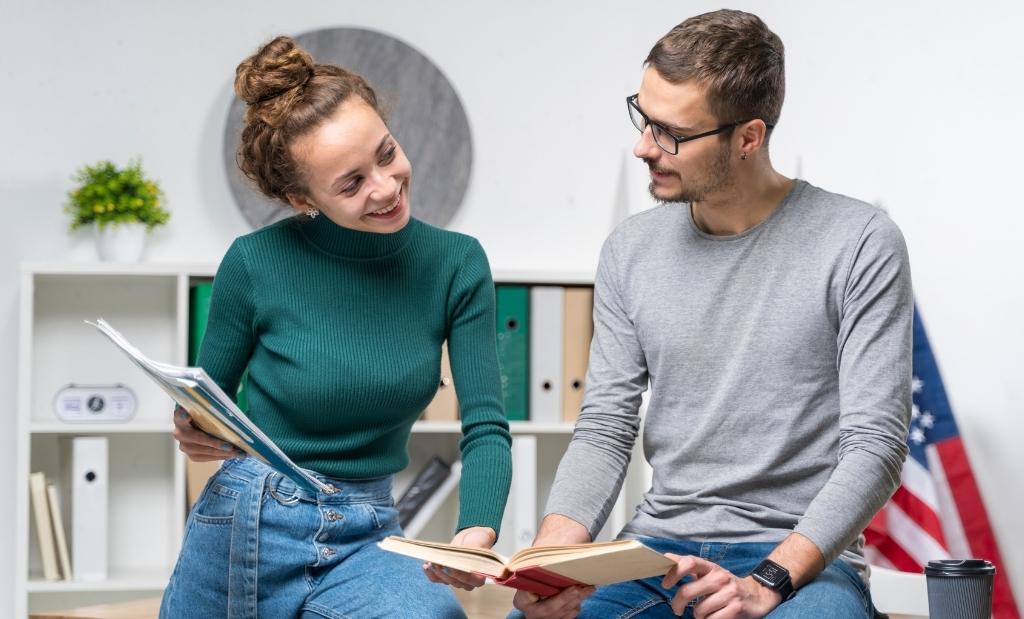 dois alunos estudando juntos em um ambiente de aprendizado, sorrindo e interagindo com livros e materiais de estudo.