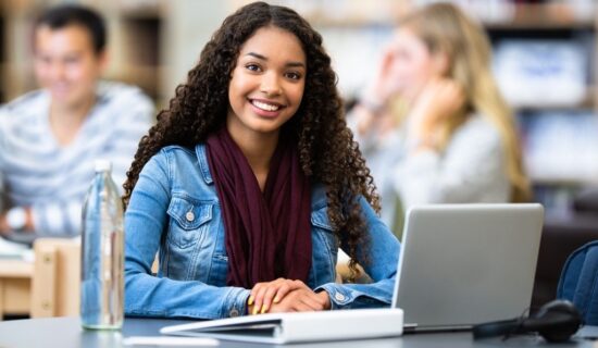 jovem estudante sorrindo enquanto usa um laptop em um ambiente escolar moderno.