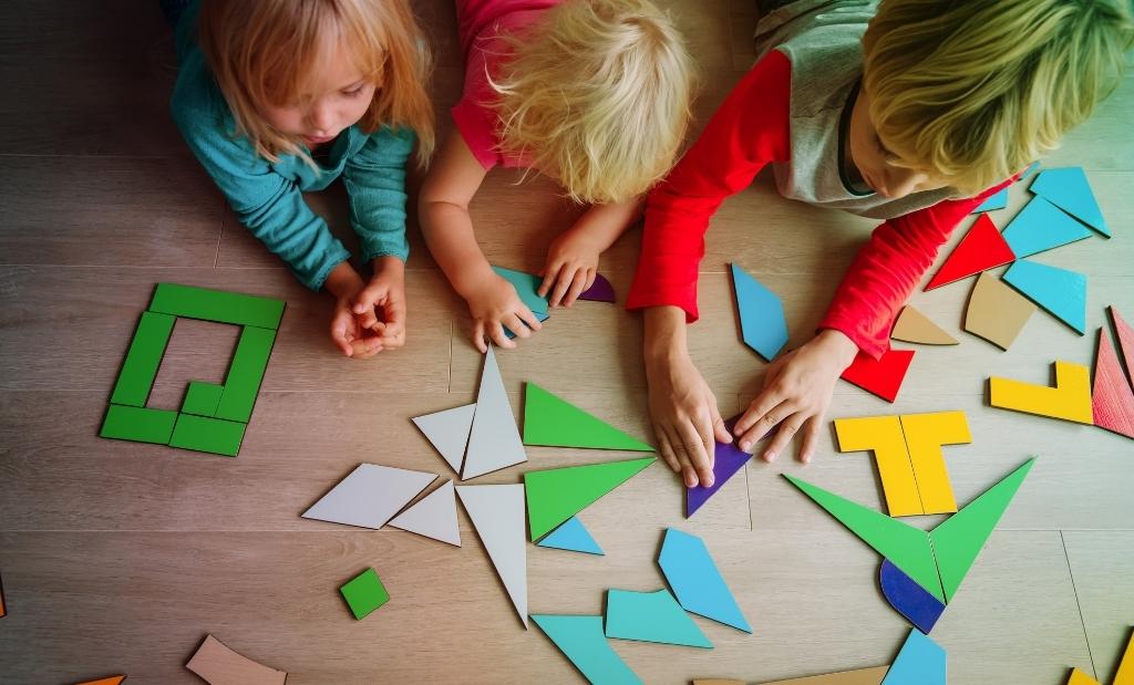 crianças montando figuras com peças coloridas no chão.